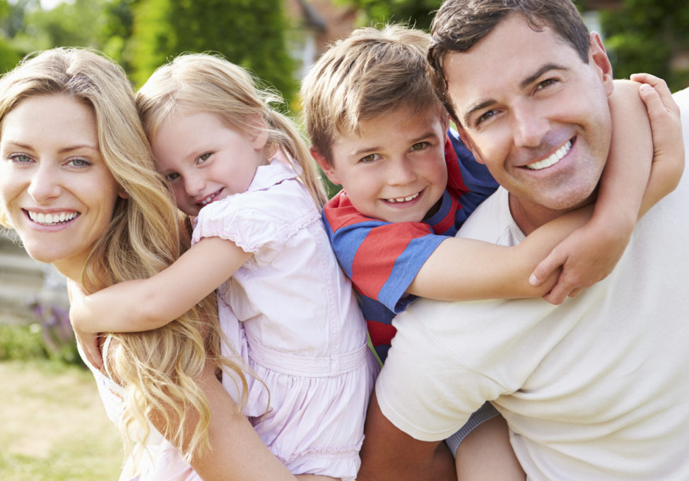 Portrait Of Happy Family In Garden Smiling At Camera